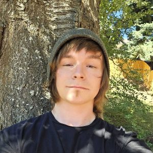 young man with light brown hair wearing a hat and a black t shirt